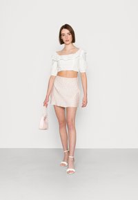 Top branco cropped com mangas rendadas, combinado com uma saia curta rosa com pequenos padrões florais. A modelo segura uma bolsa rosa clara.