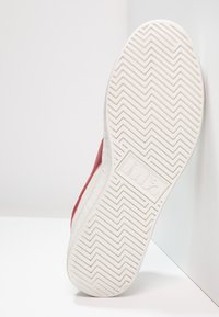 Sneaker rossa con una finitura metallica testurizzata, dotata di una suola in gomma bianca con un motivo a zigzag e un marchio in rilievo.