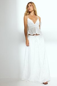 Weißes, ärmelloses Peplum-Top mit tiefem V-Ausschnitt und strukturierten Details. Kombiniert mit einem langen, weißen Rock mit Stickerei und verstellbarem Bund.