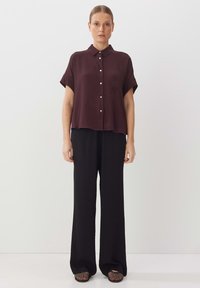 Burgundy short-sleeve shirt with a collar and silver buttons, paired with black wide-leg pants and open-toed woven black shoes.