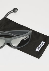 Gafas de sol grises con un diseño elegante, lentes reflectantes y un acabado mate. Acompañadas de una funda de tela negra con una etiqueta blanca.