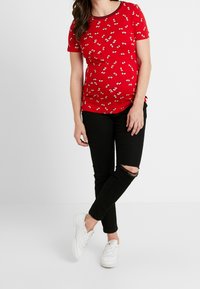 Röd bomulls-T-shirt med blommönster, korta ärmar och rund halsringning, ihop med svarta slitna jeans och vita sneakers.