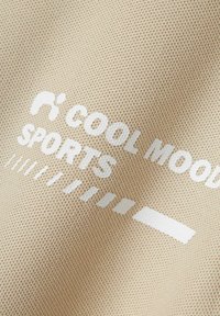Tejido beige con una superficie texturizada que presenta texto impreso en blanco "COOL MOOD SPORTS" y líneas gráficas, creando un diseño deportivo.