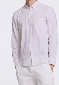 Camicia button-up a strisce sottili in tessuto chiaro con strisce verticali blu e bianche, maniche lunghe e taschino sul petto.