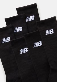 Sosete negre cu o textură ribbată, având un logo alb New Balance pe lateral. Șase perechi expuse împreună.