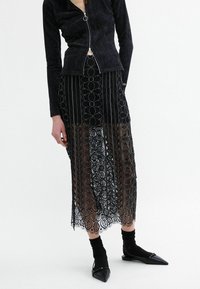 Black ribbed zip-up jacket with long sleeves paired with a black floral lace skirt and pointed-toe black flats. Hosiery is black.