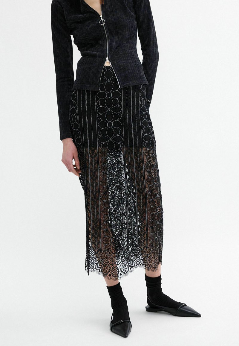 Black ribbed zip-up jacket with long sleeves paired with a black floral lace skirt and pointed-toe black flats. Hosiery is black.