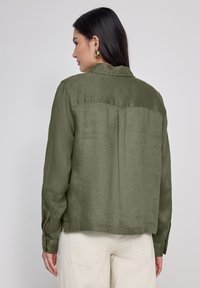 Camicia in lino verde oliva con colletto, maniche lunghe e polsini abbottonati. Presenta uno yoke sul retro e un orlo dritto. Tessuto testurizzato.