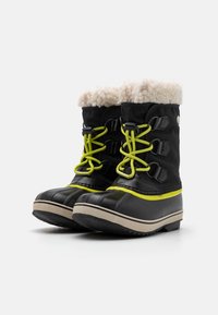 Botas de invierno negras con un suave cuello de forro polar crema, cordones amarillos y detalles. Suela de goma con agarre texturizado y material superior impermeable.