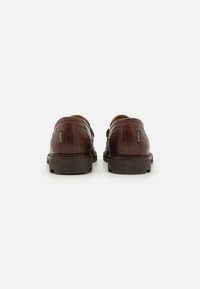 Chaussures en cuir marron avec une finition lisse, forme arrondie et semelle robuste. Comprend un branding subtil sur le côté et des coutures contrastées.