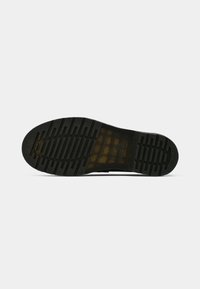 Semelle noire de chaussure avec motif de bande de roulement texturé et section semi-transparente montrant le marquage intérieur, sur fond blanc uni.