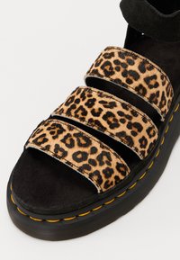 Leopardmønstrede sandaler med tre brede stropper lavet af tekstureret pels, sorte suede detaljer og en kraftig sort sål med gul syning.