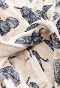 Puha bézs poláranyag sötétszürke kutyaszerű vázlatokkal, közeli kép a redőkkel és a textúra részleteivel.