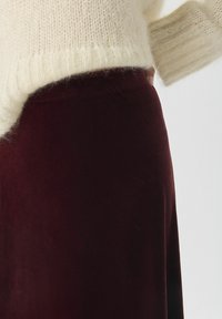 Falda de terciopelo burdeos con una textura suave, combinada con un suéter de lana crema que presenta puños acanalados y un corte XL.