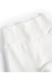 Des leggings blancs qui présentent une texture lisse et une large ceinture douce. Le tissu semble respirant et léger, sans motifs visibles.