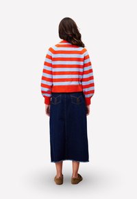 Gestreepte trui in oranje en blauwe wol, gecombineerd met een lange donkere denim rok. Heeft balloonmouwen en een geribbelde zoom. Platte slippers.