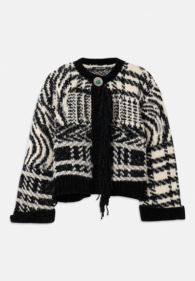 Gilet court en tricot noir et blanc avec des motifs géométriques, des franges à l'avant et un accent de bouton rond vert.