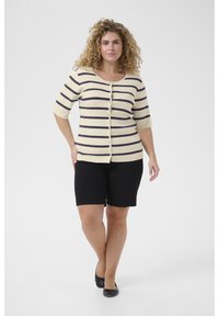 Stribet cardigan i creme med marineblå striber, med korte ærmer, rundet halsudskæring og knaplukning foran. Bruges med sorte shorts.