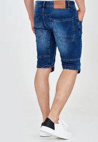 Pantaloni scurți din denim de culoare albastru deschis, cu tivuri întoarse și mai multe buzunare. Purtați cu adidași albi cu accente negre.