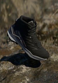 Schwarzer Wanderschuh mit hohem Knöcheldesign, strukturierter Oberseite, Schnürsenkeln und einer ausgeprägten Sohle für Traktion, mit grauen Akzenten und Branding.