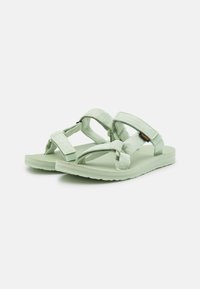 Sandalias verde claro con correas de tela texturizada, que cuentan con cierres ajustables de gancho y bucle y una suela de goma plana.