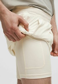 Heledadbežid spordishortid, mis on valmistatud tekstureeritud kangast, elastse vöökoha ja küljetaskuga. Sujuv ja hingav materjal.
