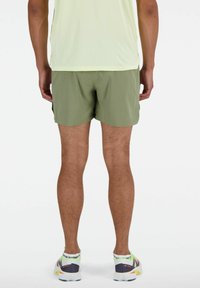 Grüne Sportshorts aus leichtem Stoff, mit elastischem Bund und seitlichen Taschen, kombiniert mit mehrfarbigen Laufschuhen.