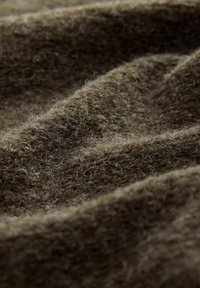 Brauner Wollstoff mit einer weichen, flauschigen Textur, der tiefe Falten aufweist, die verschiedene Licht- und Schattenmuster erzeugen.