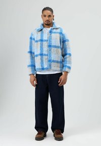 Furry jacket in light blue and cream with a check pattern, featuring a collared neck, three buttons, and long sleeves. Dark jeans and brown boots.