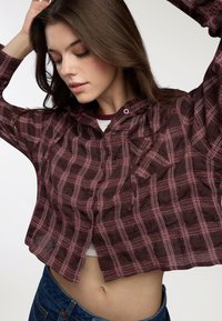 Camicia a maniche corte scozzese bordeaux con linee bianche e nere, dotata di colletto, chiusure con bottoni e tasca applicata. Tessuto texture.