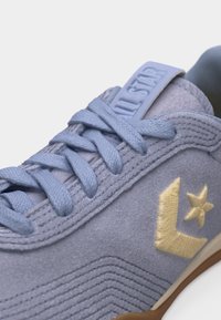 Ανοιχτό μπλε σουέτ αθλητικό παπούτσι με κορδόνια στο ίδιο χρώμα, ταμπα κεντητό αστέρι και λογότυπο σε σχήμα βέλους, και ελαστική σόλα, εμφανής σε λευκό φόντο.