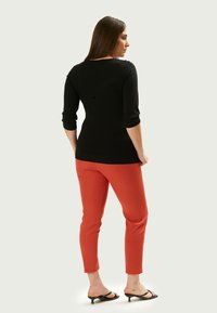 Schwarzes Stricktop mit Dreiviertelärmeln, kombiniert mit engen orangen Hosen. Auffällige Details sind der Rundhalsausschnitt und die schlanke Silhouette.