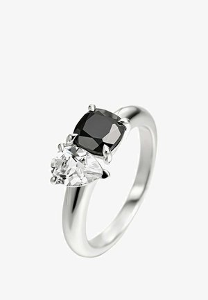 Anillo de plata con una piedra negra en forma de cojín y una piedra clara en forma de pera, ambas engastadas en garras sobre una banda pulida.