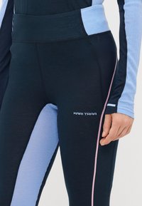 Jūrų ir šviesiai mėlyni sportiniai legginsai su tinklinėmis detalėmis, kontrastingomis siūlėmis ir subtiliu logotipu ant šlaunies. Prigludusi dizaino forma, elastinga medžiaga.