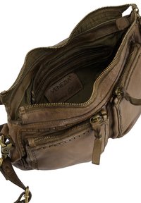 Brązowa skórzana torba crossbody z wieloma zamykanymi na zamek kieszeniami, podszewką oraz widoczną etykietą marki. Charakteryzuje się teksturowaną powierzchnią i mosiężnym okuciem.