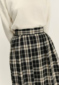 Černá a béžová kostkovaná sukně s plisovaným designem. Vyrobena z texturované tkaniny, má vysoký pás a jednotný vzor po celém povrchu.