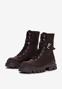 Smeđe gležnjače od teksturiranog materijala, s vezanjem sprijeda, bočnim zatvaračem, čvrstim potplatima i dekorativnim detaljem kopče.