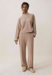 Beige lounge-set met een cropped, lange mouwen top met een mandarin kraag en brede broekspijpen met subtiele plooien, gemaakt van zachte stof.