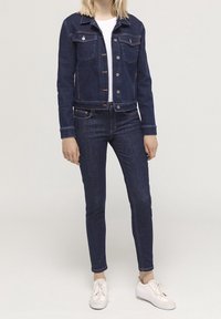 Mörkblå denimjacka med knappstängning fram, två bröstfickor och matchande mörka jeans i slim fit. En enkel vit t-shirt och ljusa sneakers fulländar looken.