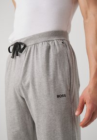 Jogging gris avec une taille élastique à cordon de serrage, des poches latérales et un logo "BOSS" noir sur la cuisse gauche. Confectionné dans un matériau doux et texturé.