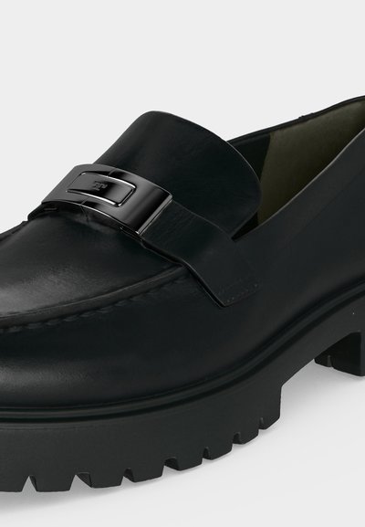 Μαύρο δερμάτινο loafer με χοντρή σόλα με ανάγλυφα και λαμπερή μεταλλική αγκράφα μπροστά.