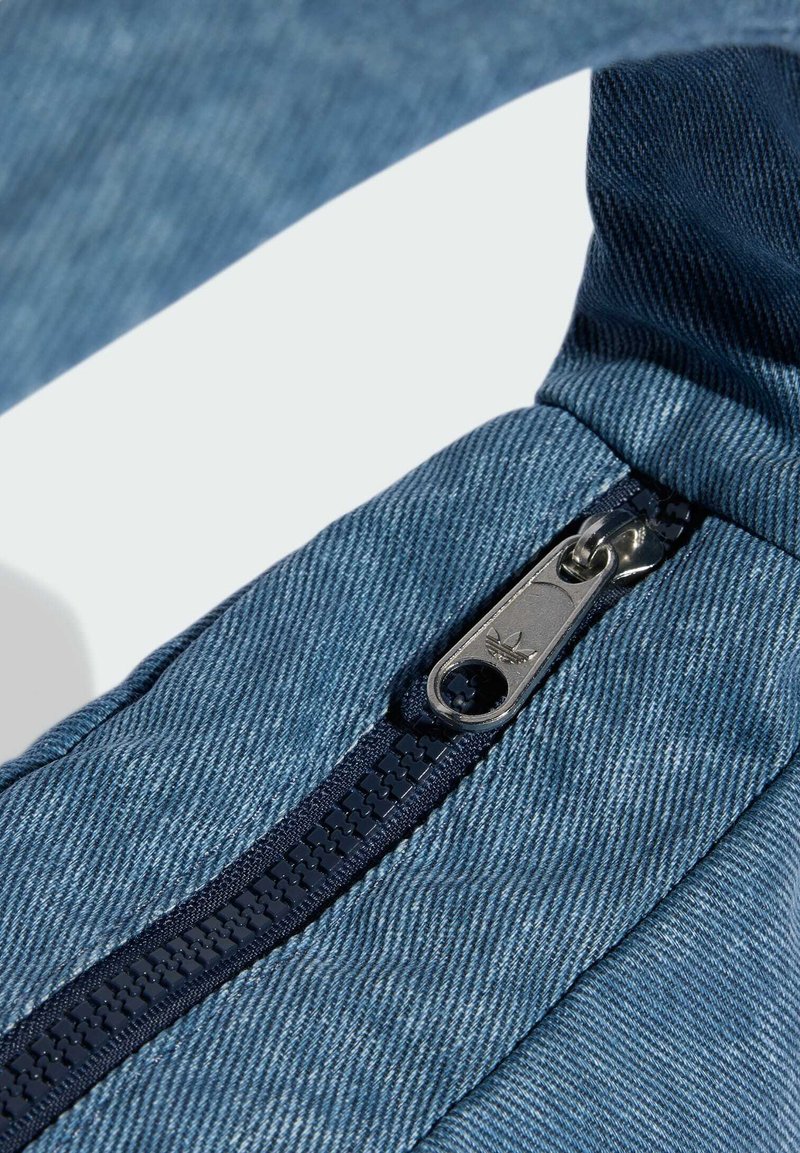 Borsa in denim blu con una cerniera blu navy, con una texture liscia e dettagli di cucitura distinti. Il cursore della cerniera ha un piccolo emblema.