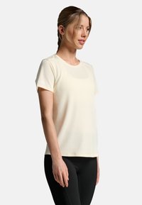 Light cream short-sleeve t-shirt made of soft fabric, featuring a round neckline and a slight sheen, paired with black leggings.