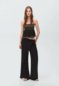 Svart strapless-topp med broderade detaljer, kombinerad med flödande svarta wrapbyxor. Lättviktigt tyg, löst snitt för komfort. Platta sandaler.