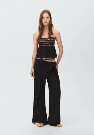 Svart strapless-topp med broderade detaljer, kombinerad med flödande svarta wrapbyxor. Lättviktigt tyg, löst snitt för komfort. Platta sandaler.