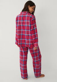 Rødt ternet pyjamasæt lavet af blødt stof, bestående af en skjorte med knapper og matchende bukser med blå accenter og en afslappet pasform.