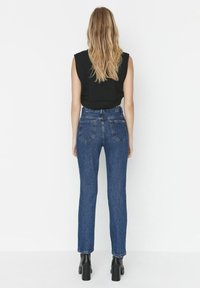 Jeans in denim blu a vita alta con taglio dritto, design a cinque tasche e leggera scoloritura, abbinati a un top senza maniche nero.