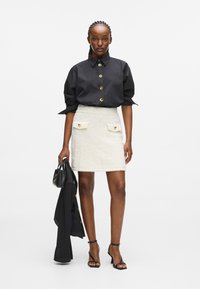 Fekete gombos ing, puffos ujjal; krémszínű tweed mini szoknya aranygombokkal; fekete magassarkú és kézitáska. Egyszerű, letisztult dizájn.