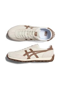 Jasno beżowe i brązowe sneakersy Onitsuka Tiger, jeden pokazany z widoku z góry, a drugi z boku, z teksturowanymi gumowymi podeszwami.