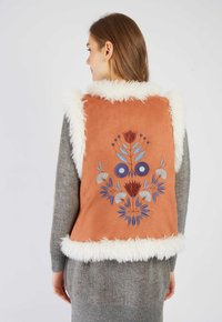 Zamszowa kamizelka w terrakotowym kolorze z białym sztucznym futrem. Posiada wielokolorowy haft kwiatowy na plecach. Teksturowany i warstwowy design.